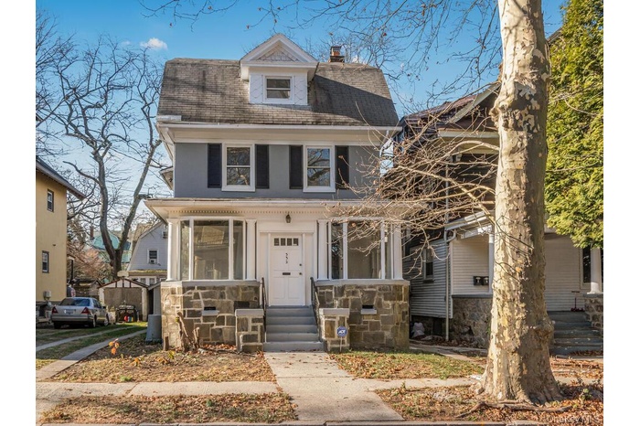 View of front facade featuring a chimney, stone siding, and a shingled roof