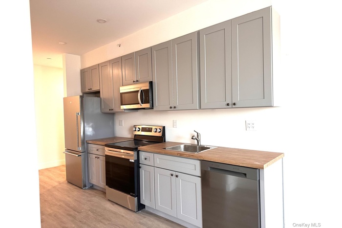 Kitchen with appliances with stainless steel finishes, light wood-type flooring, gray cabinets, butcher block countertops, and recessed lighting