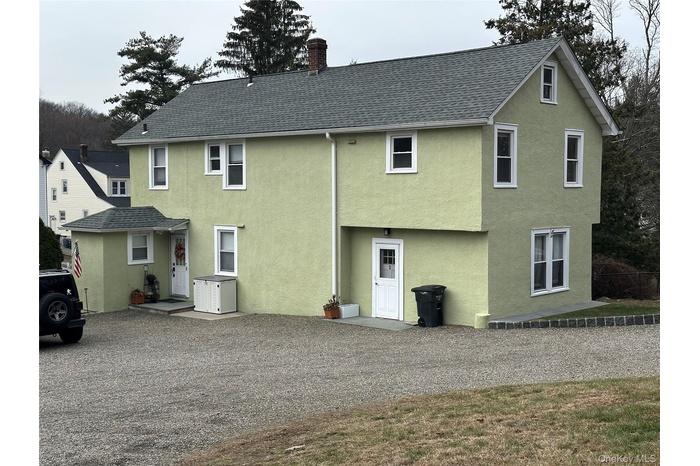 Back of house with stucco siding, a chimney, and a shingled roof