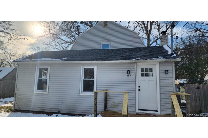 Snow covered rear of property featuring roof with shingles, a gambrel roof, and a chimney