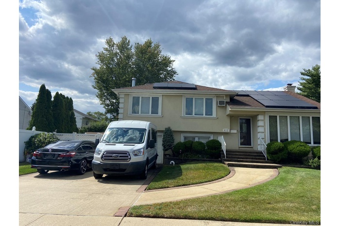 Split level home with stucco siding, solar panels, a shingled roof, a chimney, and driveway