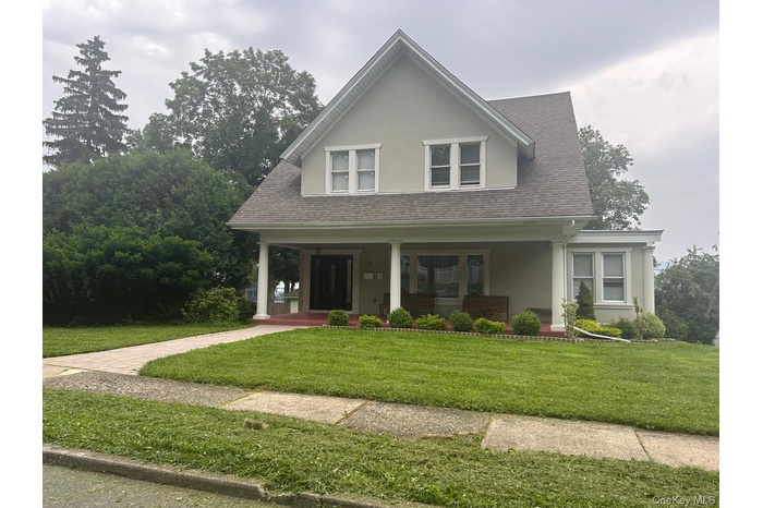 View of front of property with a porch, stucco siding, a front lawn, and a shingled roof