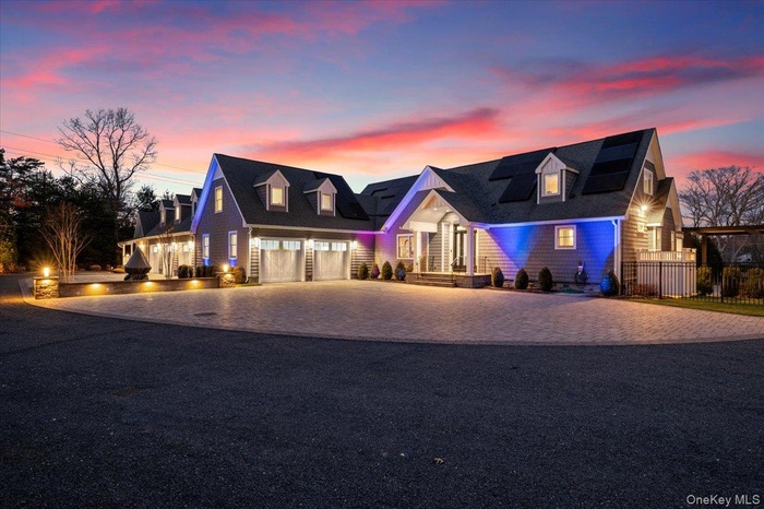 Cape cod house with decorative driveway, a garage, and roof mounted solar panels