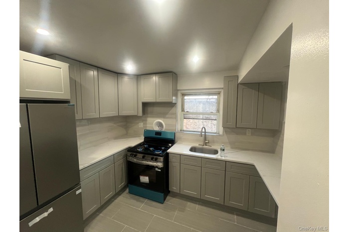 Kitchen with gray cabinets, freestanding refrigerator, range with gas stovetop, light stone countertops, and backsplash
