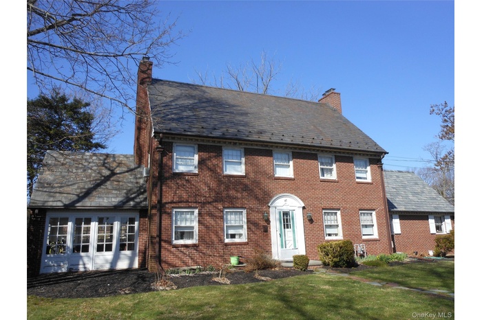 Colonial home featuring a chimney, a front lawn, a high end roof, and brick siding