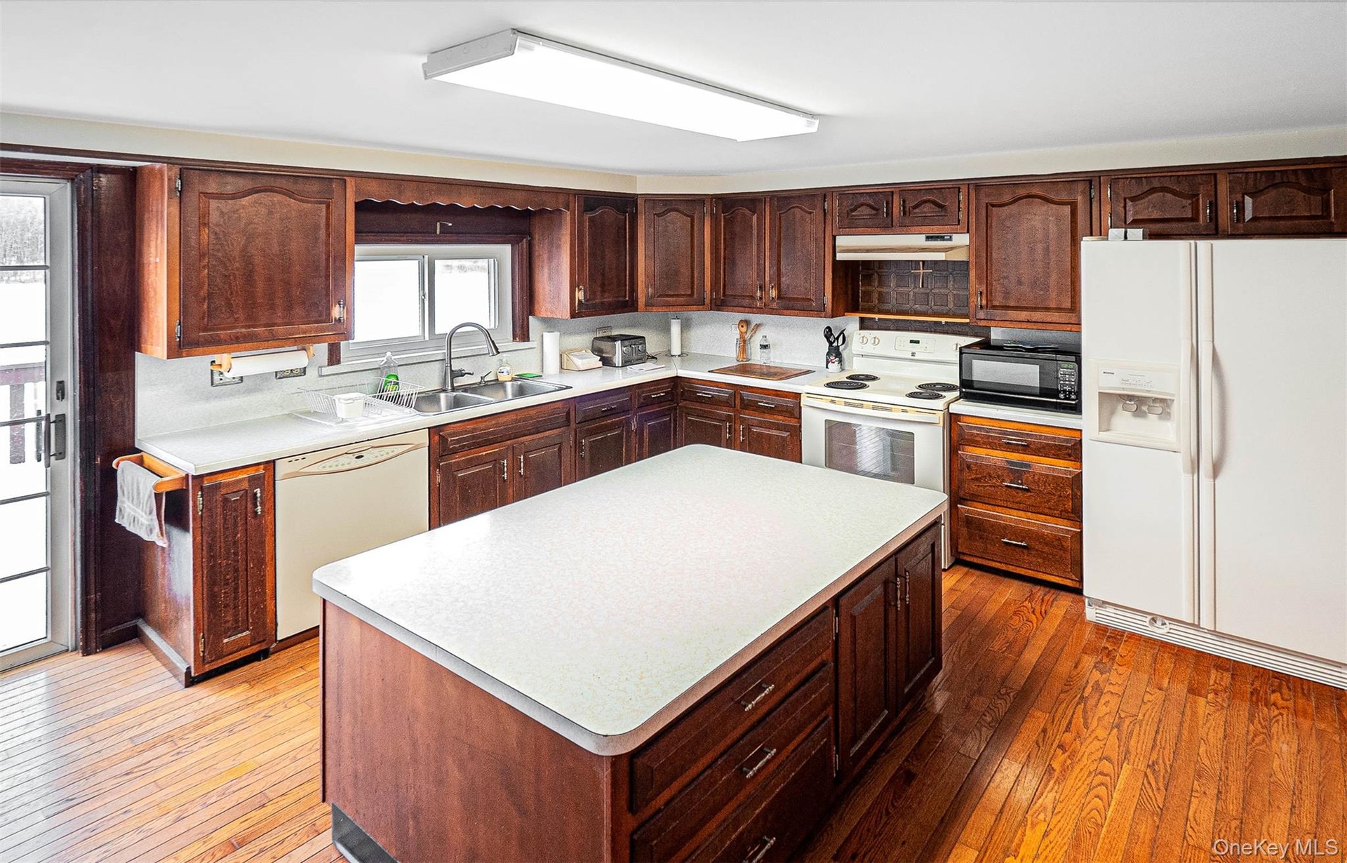 Kitchen with white appliances, dark wood-style floors, light countertops, and dark brown cabinets