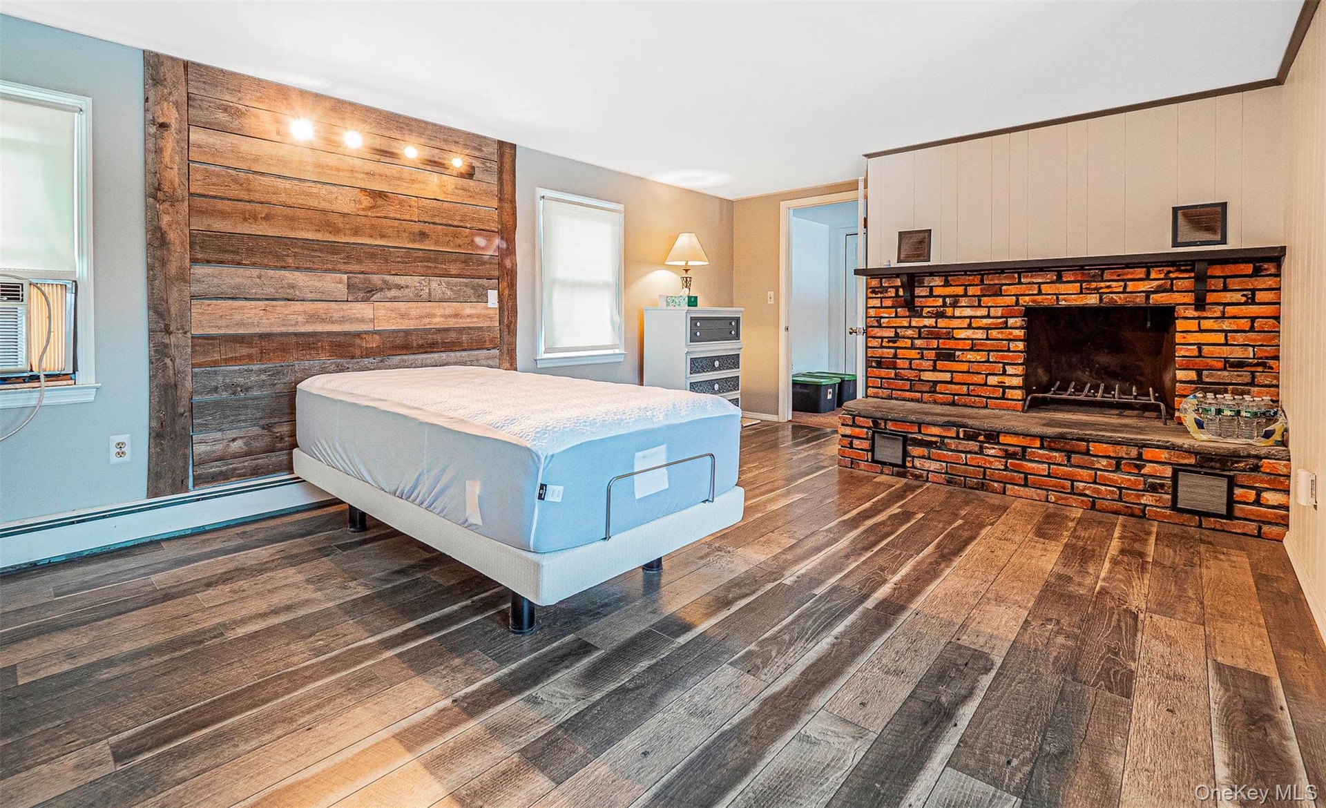 Bedroom featuring wood finished floors, a brick fireplace, an accent wall,
