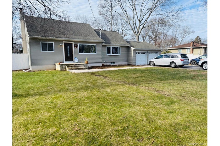 View of front of property featuring a front lawn, an attached garage, a shingled roof, and driveway
