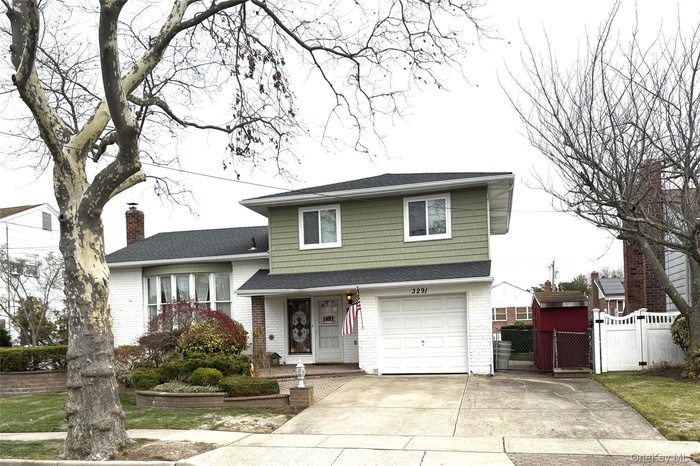 Split level home with a gate, a shingled roof, driveway, brick siding, and a garage