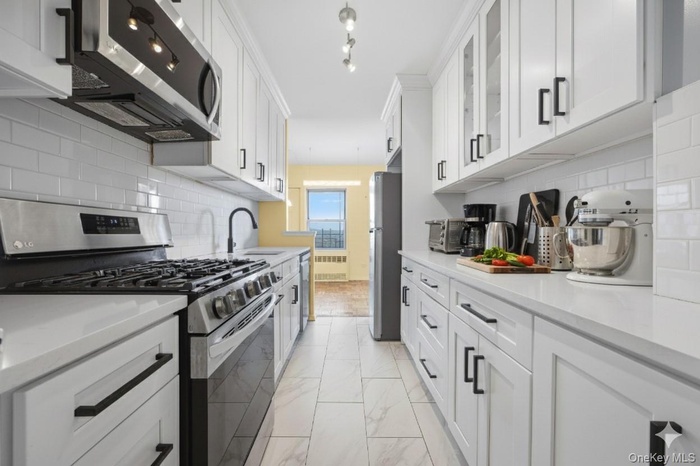 Kitchen with appliances with stainless steel finishes, white cabinets, backsplash, light marble finish flooring, and light stone counters