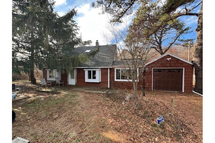 Ranch-style home featuring a garage, a chimney, a patio, and roof with shingles