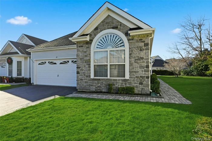 Ranch-style house featuring stone siding, a front lawn, driveway, and a garage