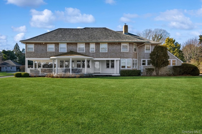 Rear view of property featuring a lawn, a chimney, covered porch, and roof with shingles