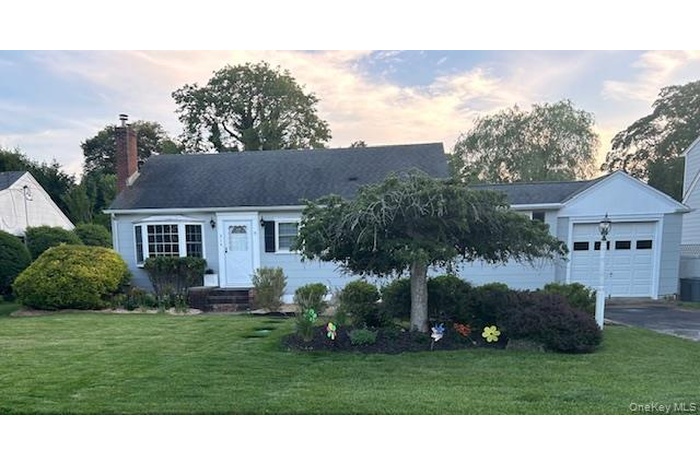 View of front of property featuring a lawn, an attached garage, a chimney, and driveway