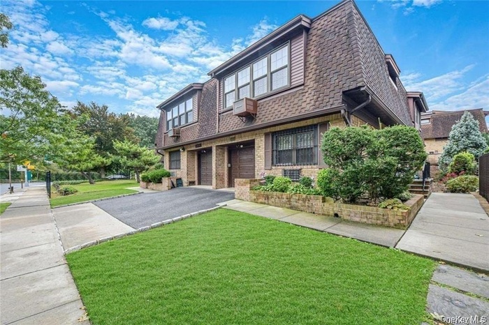 View of front facade featuring a front yard, driveway, mansard roof, and a garage