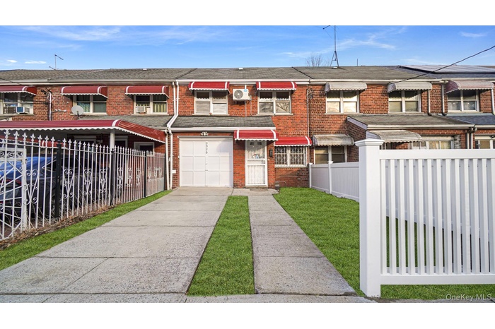 Traditional-style house featuring a fenced front yard, roof with shingles, driveway, and brick siding