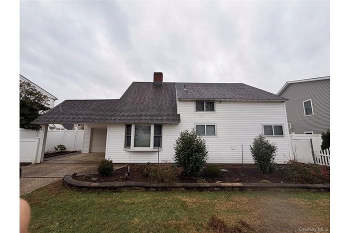 Rear view of house with a shingled roof, a chimney, driveway, and an attached garage