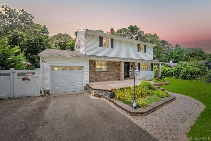 Traditional-style home with a garage, asphalt driveway, stone siding, a gate, and a chimney
