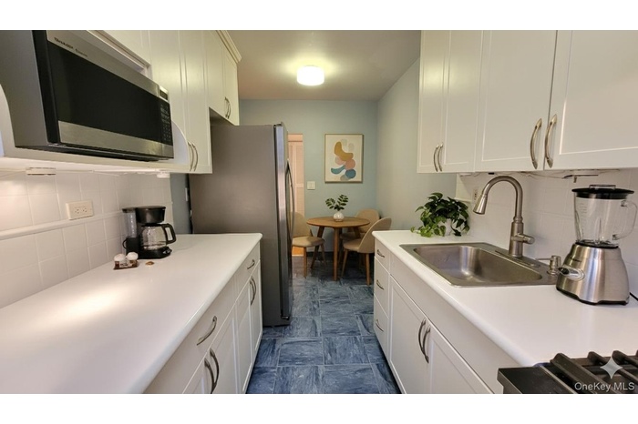 Kitchen with tasteful backsplash, appliances with stainless steel finishes, white cabinetry, and light countertops