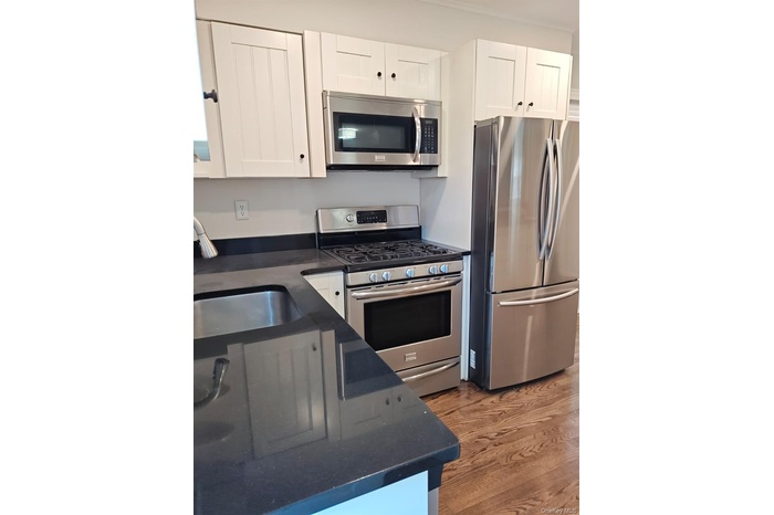 Kitchen featuring stainless steel appliances, white cabinets, light wood-type flooring, and dark stone countertops