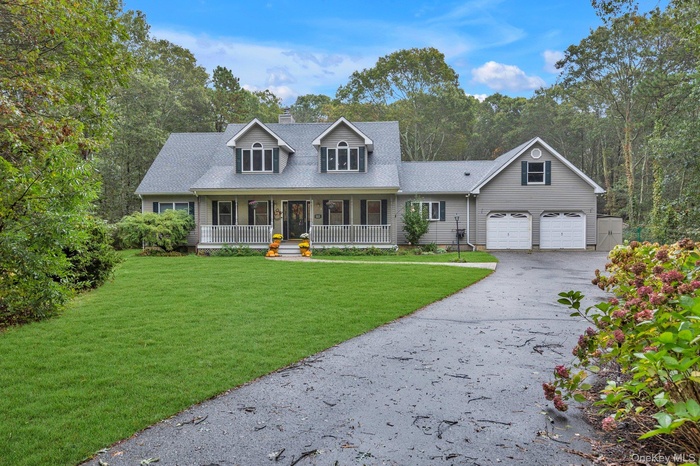 Cape cod-style house with covered porch, a front yard, driveway, a chimney, and a garage