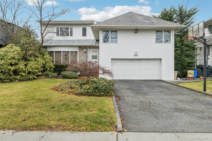 View of front of home with roof with shingles, driveway, a front lawn, and a sunroom