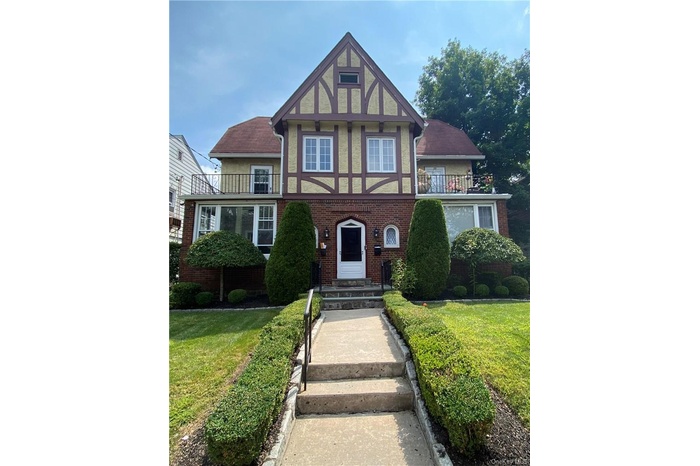 Tudor house featuring a balcony and a front lawn