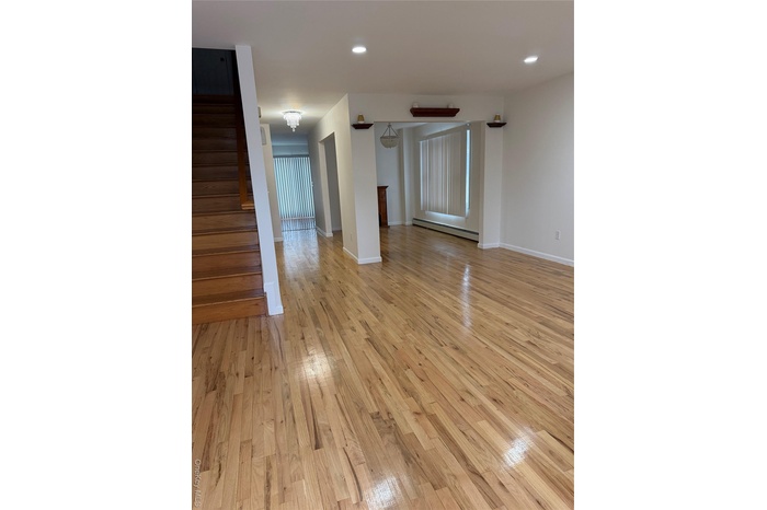 Unfurnished living room with light wood-style flooring, stairway, a baseboard radiator, recessed lighting, and a chandelier