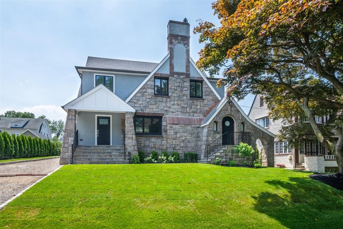 Tudor-style house with stucco siding, stone siding, a front yard, and a chimney