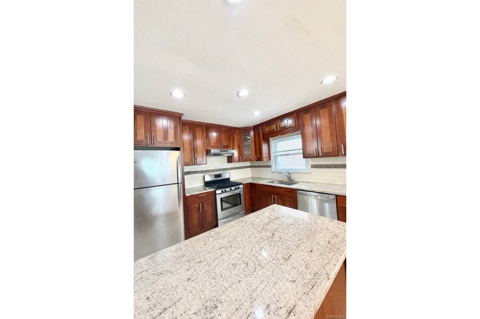 Kitchen featuring stainless steel appliances, tasteful backsplash, light stone countertops, glass insert cabinets, and recessed lighting