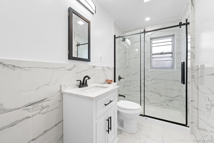 Full bathroom featuring tile walls, wainscoting, light marble finish floors, vanity, and a marble finish shower