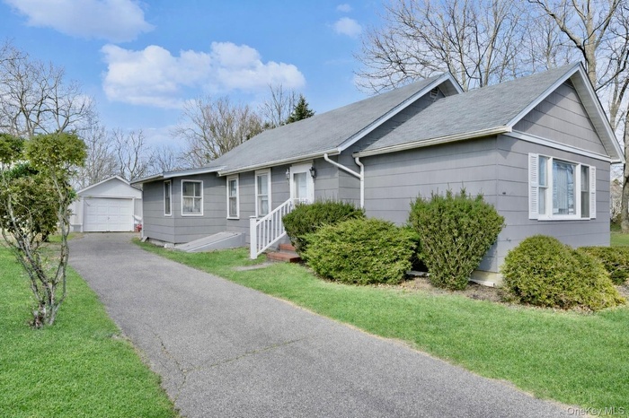 Ranch-style house with a detached garage, an outdoor structure, driveway, and a front lawn