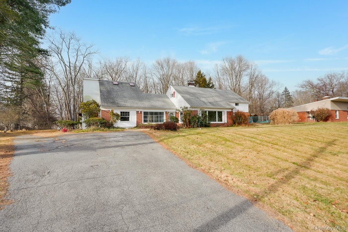 Cape cod house featuring brick siding, a front lawn, a chimney, driveway, and a shingled roof