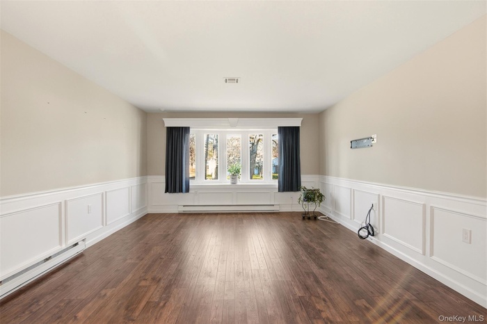 Empty room featuring a baseboard heating unit, dark wood-style floors, and a wainscoted wall