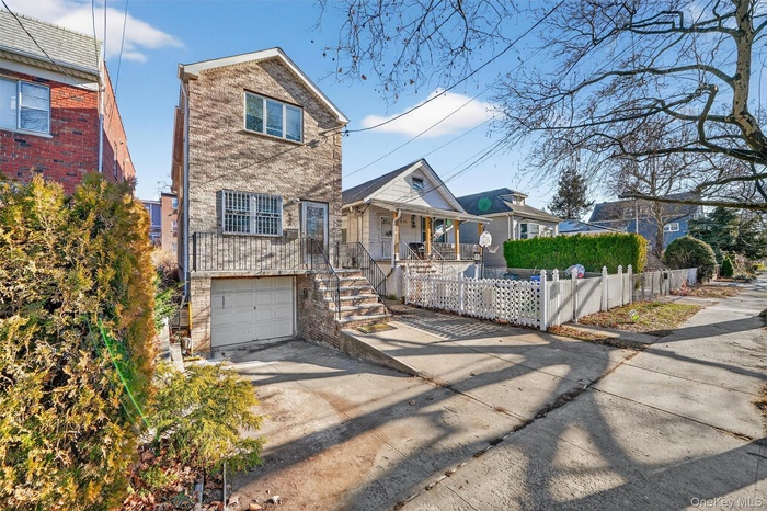View of front of home featuring driveway, a fenced front yard, a garage, stairs, and covered porch