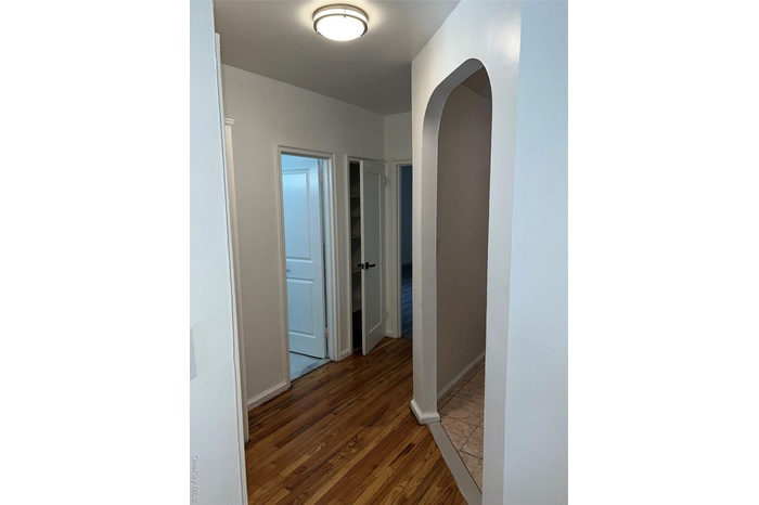Hallway featuring arched walkways and light wood finished floors
