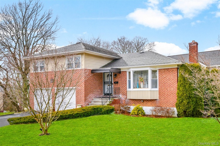 Tri-level home featuring a front lawn, brick siding, asphalt driveway, and a garage