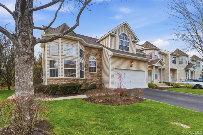 Traditional-style house featuring stone siding, a front lawn, driveway, an attached garage, and a shingled roof