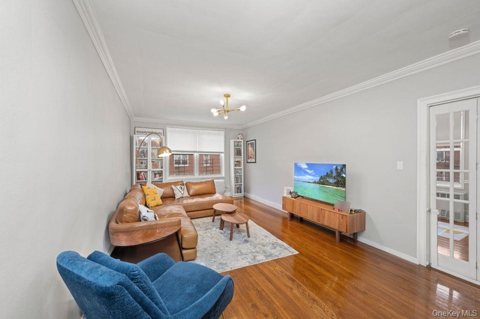 Living room featuring crown molding, dark wood-style flooring, and a chandelier
