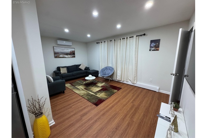 Living room with wood finished floors, recessed lighting, baseboard heating, and a wall mounted air conditioner