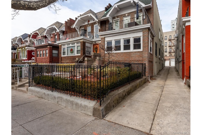 View of front of house with brick siding, a residential view, a balcony, and a fenced front yard