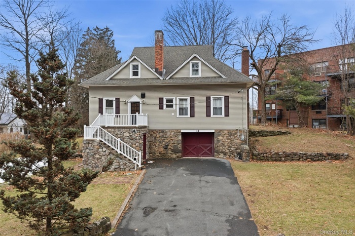 View of front of property featuring driveway, stone siding, a shingled roof, and a front lawn