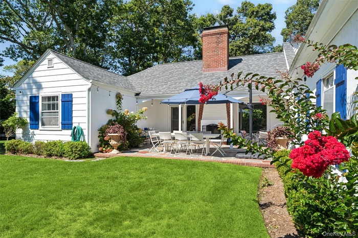 Back of house with a shingled roof, a patio, a chimney, and a lawn