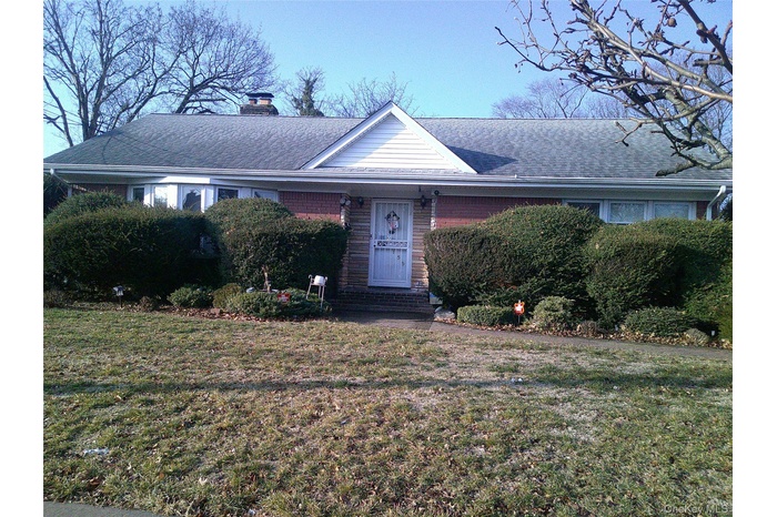 View of front of home featuring a shingled roof, a front yard, a chimney, and brick siding