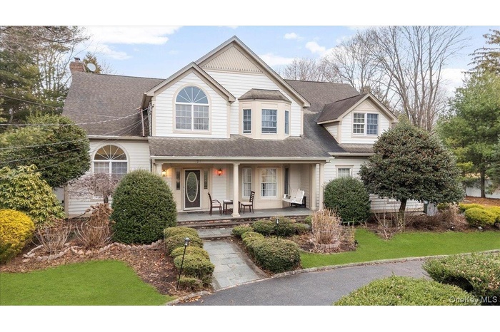View of front of home with a porch, roof with shingles, a front lawn, and a chimney