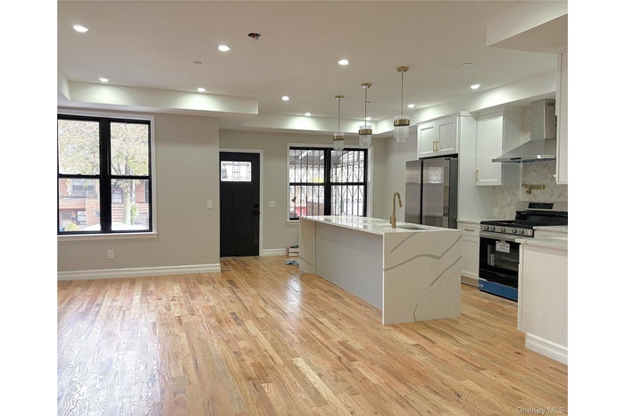 Kitchen with appliances with stainless steel finishes, wall chimney exhaust hood, recessed lighting, hanging light fixtures, and an island with sink