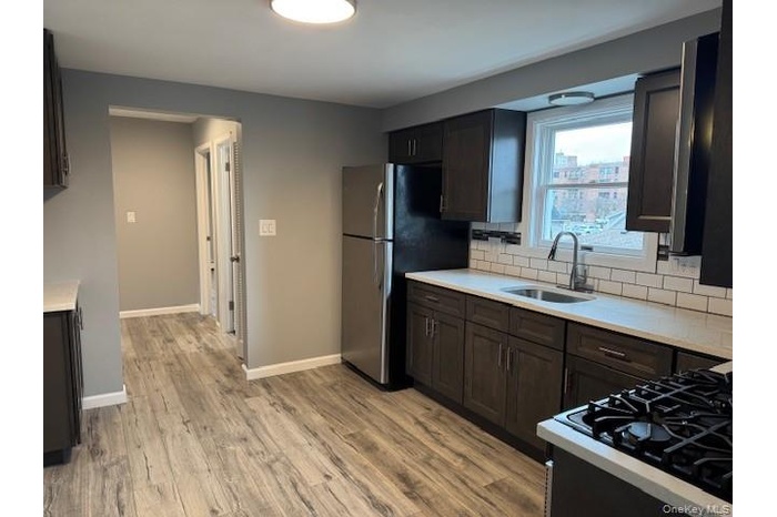 Kitchen featuring dark brown cabinets, tasteful backsplash, light wood finished floors, appliances with stainless steel finishes, and light stone coun