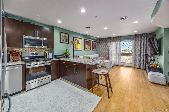 Kitchen featuring dark brown cabinetry, a peninsula, appliances with stainless steel finishes, light stone countertops, and recessed lighting