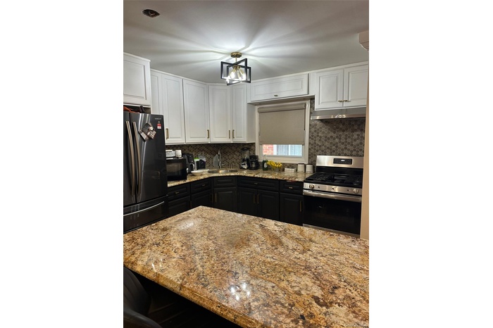 Kitchen featuring black appliances, light stone counters, white cabinets, a chandelier, and backsplash