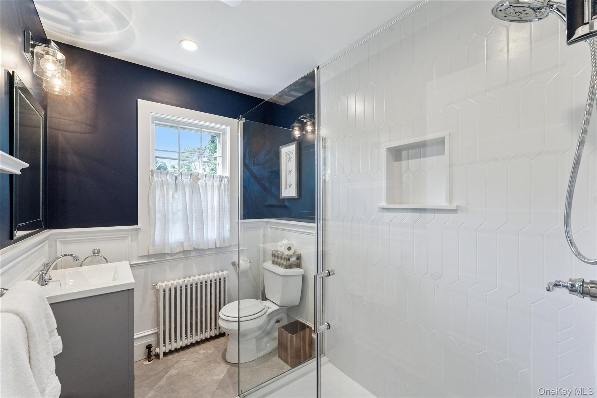 Bathroom featuring a shower stall, vanity, radiator heating unit, a wainscoted wall, and recessed lighting
